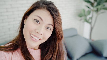 Asian blogger woman using smartphone recording vlog video in living room at home,female enjoy funny moment while lying on the sofa when relax at home. Lifestyle blogger making video at home.