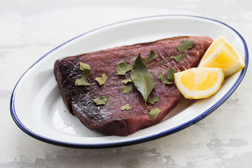 raw tuna with lemon and bay leaf on ceramic background