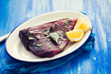 raw tuna with lemon and bay leaf on ceramic background