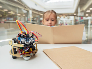 A cute girl constructs metal robot and program it. The boards and microcontrollers are on the...