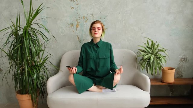 Young woman meditates at home while holding smartphone