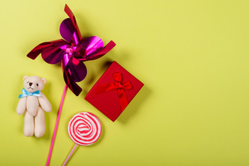 Pinwheel, teddy bear, lollipop and gift on neon green background. Space for text on the right side of the image.