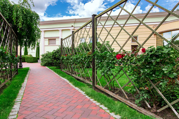a footpath made of paving slabs surrounded by a green lawn and a fence for a winding shrub rose in...