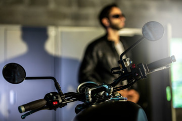  Biker in a leather jacket resting on the bike in the dark.