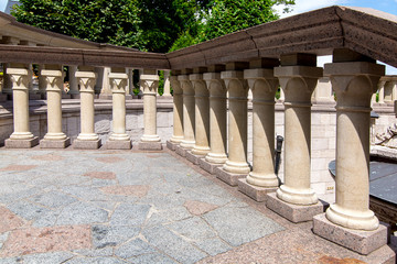 Fototapeta premium a balcony with stone tiles on the floor and a railing with a balustrade lit by sunlight in the background are green trees.