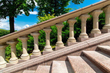 Fototapeta na wymiar stone railing with balustrades at the marble staircase in the garden with green plants on a sunny day with a blue sky, nobody.