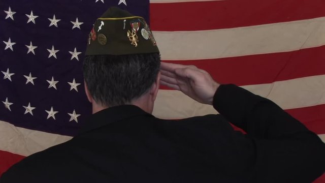 A man in a VFW cap walking up to and old faded 48 star American flag and saluting