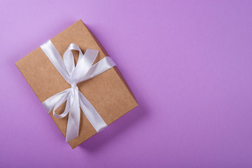 Gift box with bow over purple neon background. Space for text on the right side of the image.