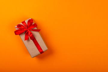 Gift box with bow over orange background. Space for text on the right side of the image.
