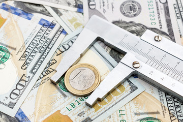 Vernier caliper with coin of one euro on background of dollar bills. Exchange rate by euro to dollar.