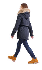 Back view of going woman in jeans and winter jacket.