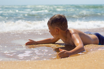 Fototapeta na wymiar A child plays lying on the sea sandy shore