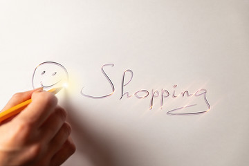Female hand with yellow pencil is drawing happy smile on the white paper sheet. There is written word "Shopping". Yellow bright lines. White background. Buy Nothing Day.