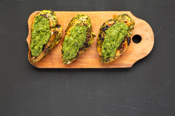 Grilled chimichurri chicken breast on a rustic wooden board on a black background, top view. Flat lay, overhead, from above. Copy space.