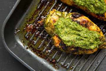 Grilled chimichurri chicken breast in a grilling pan on a black surface, top view. Flat lay, overhead, from above. Close-up.