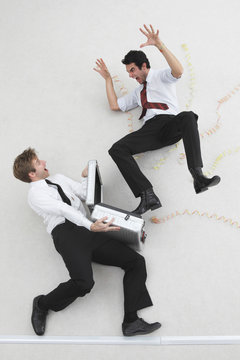 Two businessmen, one holding suitcase, the other scaring him, elevated view