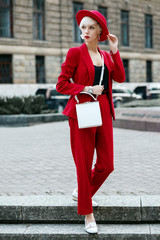 Outdoor full-length street fashion portrait of young blonde woman wearing total red look, suit,...