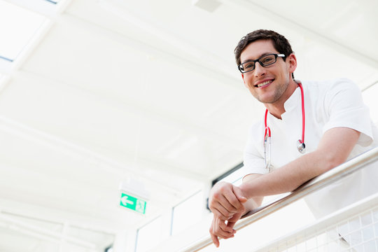 Germany, Bavaria, Diessen am Ammersee, Young doctor with stethoscope leaning on railing, smiling, portrait