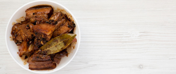 Homemade Filipino Adobo Pork in a white bowl over white wooden background, top view. Flat lay, from above, overhead. Copy space.