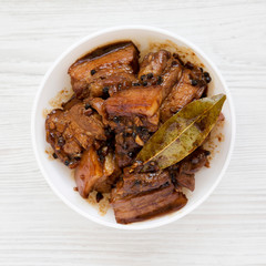 Homemade Filipino Adobo Pork on a white wooden surface, overhead view. Flat lay, from above, top view.