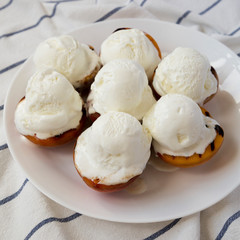 Homemade grilled peaches with vanilla ice cream on a white plate, side view. Close-up.