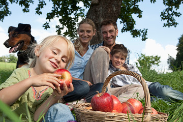 Germany, Bavaria, Altenthann, Girl with basket of apples, family with dog in background