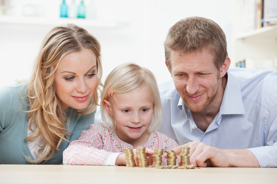 Germany, Bavaria, Munich, Parents and daughter counting coins at table, smiling