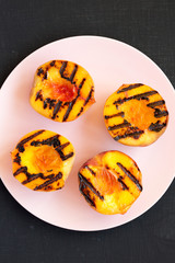 Top view, homemade grilled peaches on a pink plate on a black background. Flat lay, overhead, from above. Close-up.