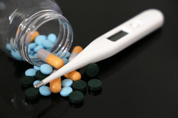 Pills in a bottle, medication in capsules and digital thermometer on a dark glass table. Concept of...