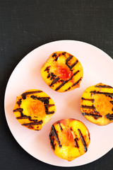 Homemade grilled peaches on a pink plate on a black background, top view. Flat lay, overhead, from above.