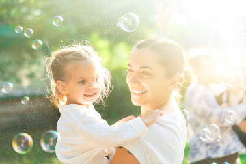 Little  lovely girl and her mother having fun with soap bubbles on blurred nature background....