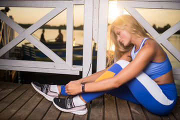 Beautiful smiling girl in sportswear posing at sunset near the lake