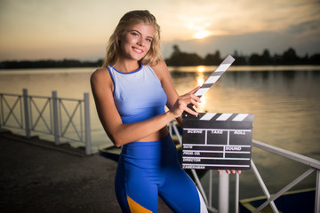 Beautiful smiling girl in sportswear with a clapperboard in her hands