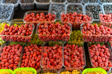 Fototapeta na wymiar Bright juicy red raspberries in a plastic container on a store counter.
