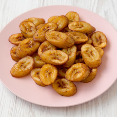 Homemade fried plantains on a pink plate on a white wooden background, side view. Close-up.
