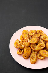 Homemade fried plantains on a pink plate on a black background, low angle view. Copy space.