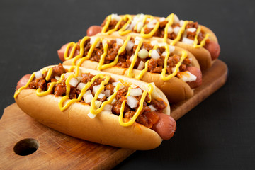 Homemade Detroit style chili dog on a rustic wooden board on a black background, low angle view....