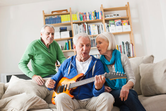 Germany, Leipzig, Senior man playing electric guitar, man and woman sitting besides