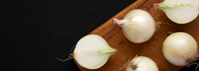 Raw white onions on a rustic board on a black background, overhead view. Flat lay, top view, from above. Space for text. - obrazy, fototapety, plakaty