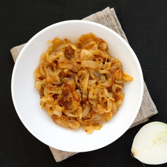 Homemade caramelized onions on a white plate on a black background, overhead view. From above, top view, flat lay. Close-up.