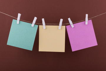 green, yellow and pink notebook paper sheets for notes and reminders, fastened with decorative red clothespins, hang on a rope against a light green background