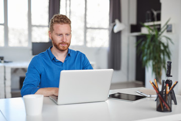 Young Caucasian employee sitting in office and typing on laptop. Start up business concept.