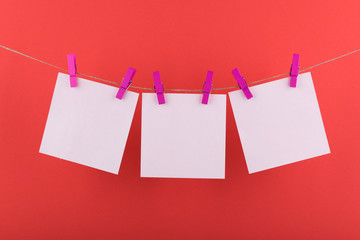 white sheets of notepad for notes and reminders, fastened with decorative lilac clothespins, hang on a rope on a red background