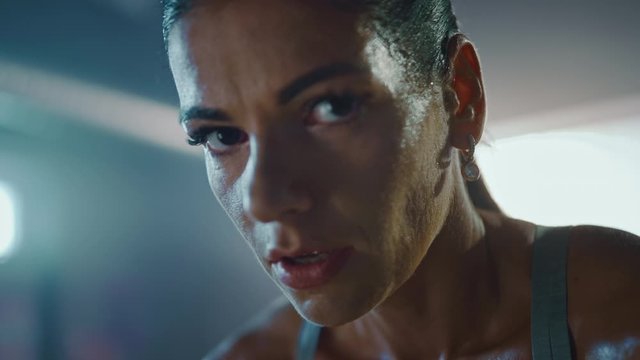 Close Up Portrait of a Beautiful Strong Fit Brunette Wiping Sweat from Her Face in a Loft Industrial Gym with Motivational Posters. She's Catching Her Breath after Intense Fitness Training Workout.