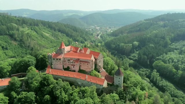 Aerial View of Fabulous Medieval Pernstejn Castle (hrad Pernstejn) in Mountain Forest in Czech Republic, Europe on Sunny Summer Day with Town and River at Background. 4K Bird's-eye view Zoom Shot