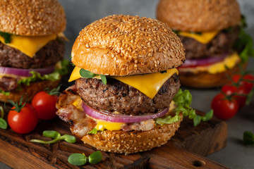 A set of homemade delicious burgers of beef, bacon, cheese, lettuce and tomatoes on a light concrete background. Fat unhealthy food close-up