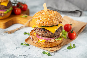 A set of homemade delicious burgers of beef, bacon, cheese, lettuce and tomatoes on a light concrete background. Fat unhealthy food close-up