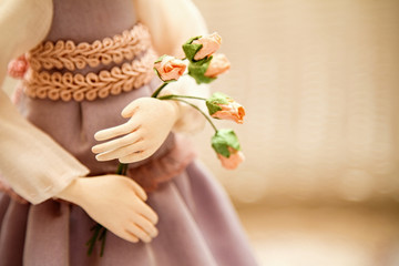 Obraz na płótnie Canvas Photo in delicate pastel colors. Doll's hands holding a bouquet with roses with blurred background