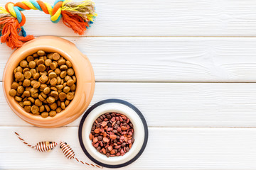 Cat and dog dry food in bowl and toys on white wooden background top view mock-up