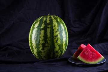 Watermelon on black cloth. Whole watermelon on dark background. Healthy food for vegan. Copy space